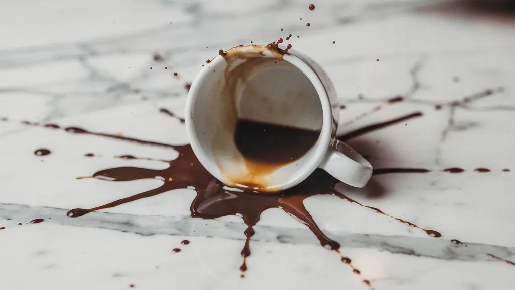 Gros plan sur une tasse de café renversée sur une surface en marbre, avec des gouttes formant un motif expressif, évoquant la maladresse charmante